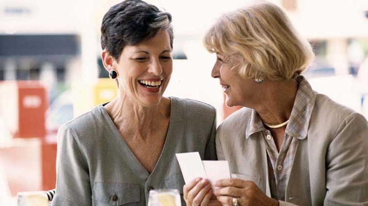 Two older women having a happy conversation while looking at cards.